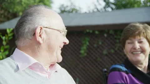 Mature couple of retirement age sharing a joke together sitting in their garden Stock Footage