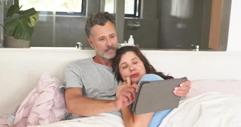 Mature couple sitting in bed sharing tablet after notification, man tapping Stock Footage 336658694