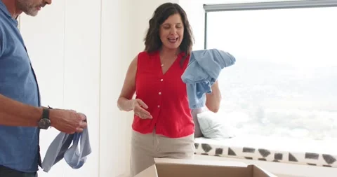 Mature couple sorting and folding light-blue shirts on bed, placing stacks into 動画素材 335575143