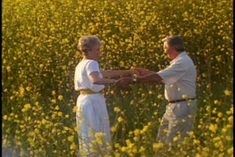 A mature couple spin while holding hands in a field of yellow wildflowers. Stock Footage 10578977