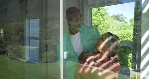 Mature couple standing behind sliding glass door holding close watching yard as Vidéo 342928076