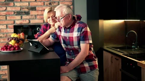 Mature couple with tablet computer sitting  in the kitchen Stock Footage 108456275