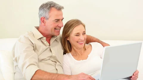Mature couple using laptop together on the couch Stock Footage 34682834