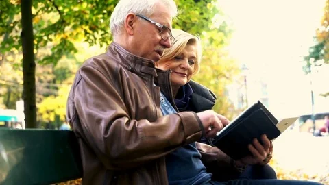 Mature couple using smartphone and tablet computer sitting on a bench in the cit Vídeo Stock 81974422