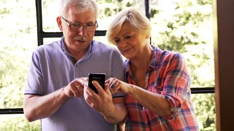 Mature couple using smartphone standing by the window at home Stock Footage 78763703