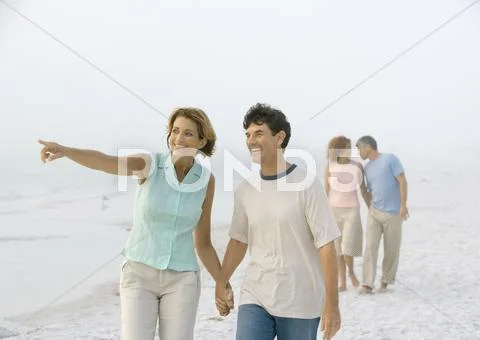 Mature Couple Walking On Beach, Woman Pointing To Distance