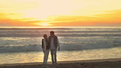 Mature couple walking on a sandy beach at sunset Stock Footage 330121380