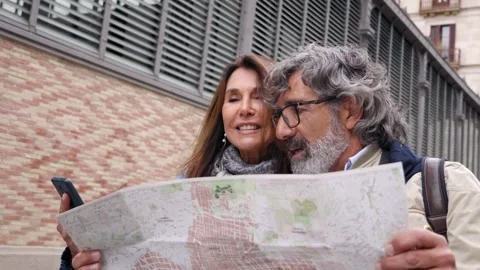 Mature couple walking talking looking at map and using mobile phone location in Stock Footage 246714443
