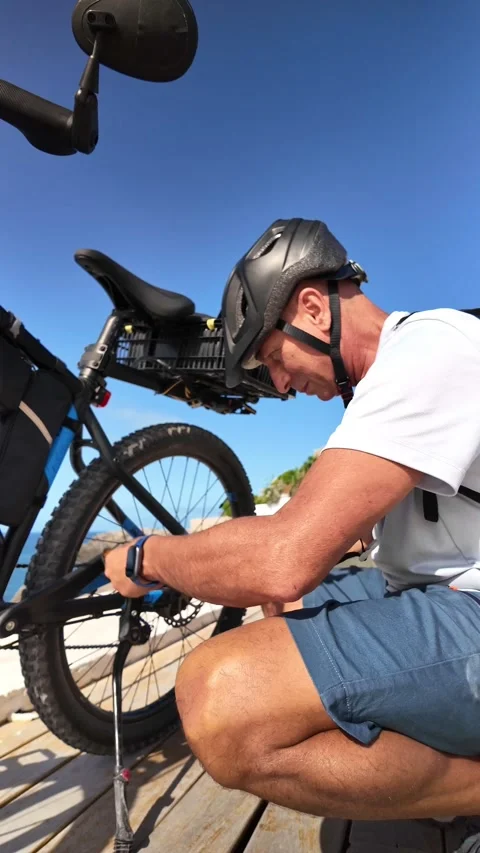 Mature cyclist maintaining his e-bike on a boardwalk Stock Footage 344816302