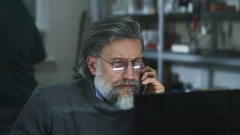 Mature designer reading data from computer during phone conversation Video stock 168636053