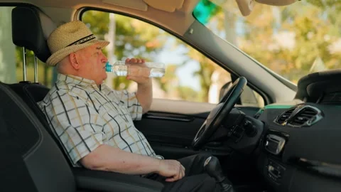 Mature driver drinking fresh water from a plastic bottle in the sunny car. 库存影片 343264450