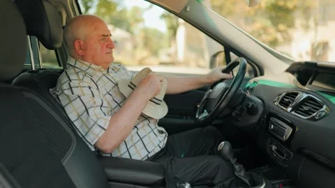 Mature driver feeling hot and fanning himself with a hat inside the summer car. Stockbeeldmateriaal 343264155