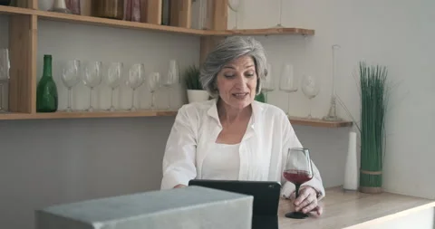 Mature elderly 60 year old woman standing with a tablet, drinking wine and Stock Footage 159167062