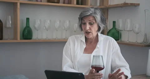 Mature elderly 60 year old woman standing with a tablet, drinking wine and Video stock 159168397
