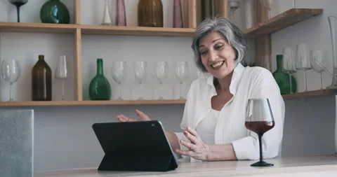 Mature elderly 60 year old woman standing with a tablet, drinking wine and Stock Footage 159171905