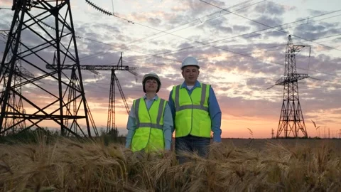 Mature electrician marks points on tablet with trainee against power lines Stock Footage 279427703