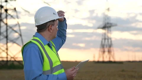 Mature engineer inputs data on tablet and looks back at power transmission line Stock Footage 278010709