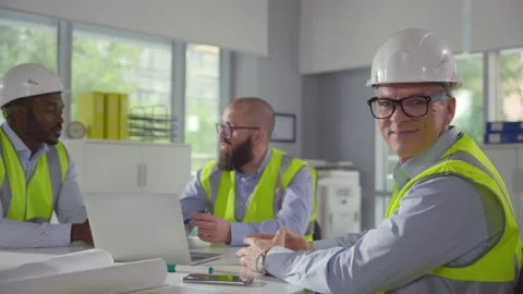 Mature engineer smiling at camera sitting at desk with colleagues Stock Footage 161009108