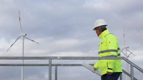 Mature engineer standing in front of a wind turbine with blueprint in his han Stock Footage 142020119