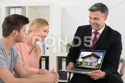 Mature Estate Agent Showing House On Laptop To Young Couple Stock Photos