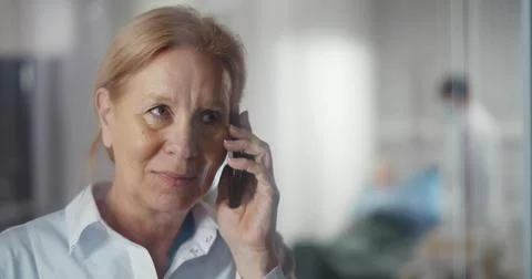 Mature female doctor standing near window and having phone call in hospital Stock Photos