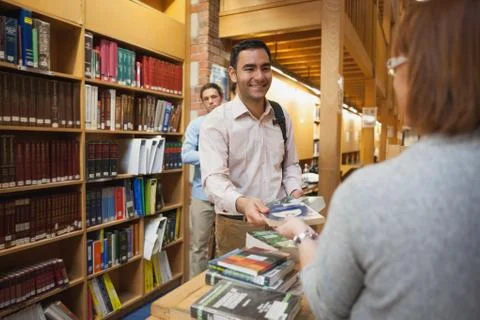 Mature female librarian handing a book to young man Stock Photos