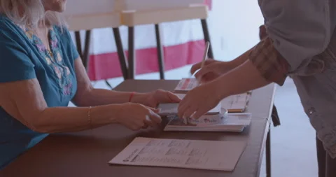 Mature female poll worker processing a young voter with a digital tablet Stock Footage 274982093