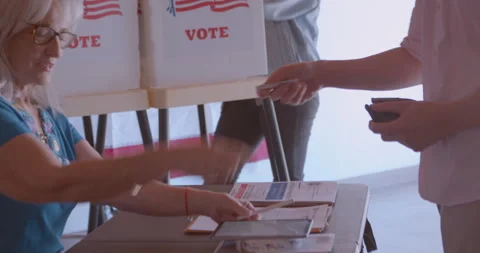 A mature female poll worker processing a male voter with a digital tablet Stock Footage 274982115