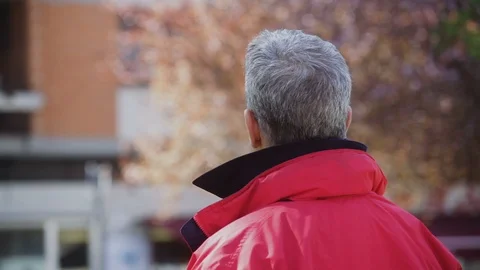 A Mature gray-Haired Man in a red jacket looks around and puts on sunglasses Stock Footage 100946019