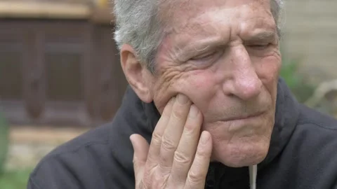Mature gray haired man touching cheek because of painful toothache indoors Stock Footage 334776107