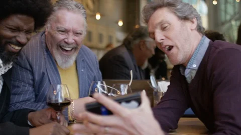 Mature group of men in a wine bar looking at a cell phone together and laughing Stock Footage