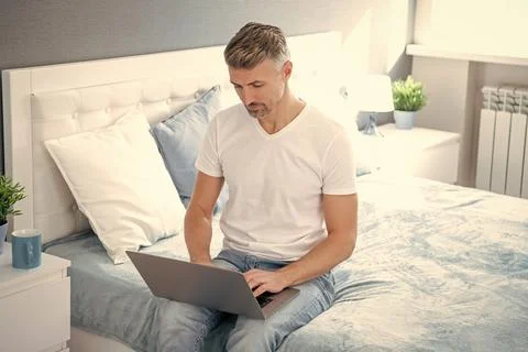 Mature guy using computer in bed with coffee Stock Photos