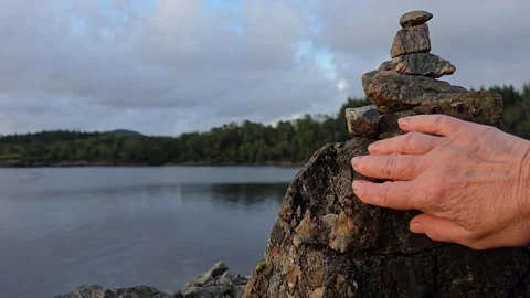 Mature hand carefully building a balancing stone tower Stock Footage 341895586