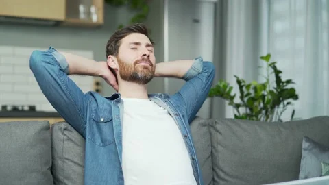 Mature handsome man stretching while sitting on sofa at home. A middle-aged man  Stock Footage 231233972
