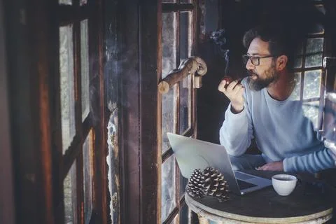 Mature hipster man use computer laptop at home in chalet wooden house smoking Stock Photos