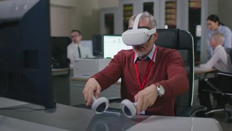 Mature it programmer put on vr goggles and take controllers working at desk on Stock Footage 198826613