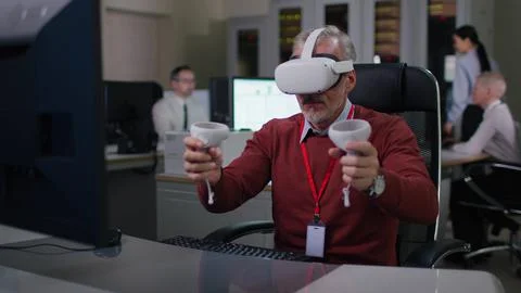 Mature it programmer put on vr goggles and take controllers working at desk on Stock Photos
