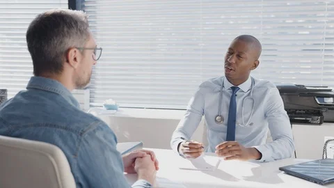Mature Male Patient Sitting At Desk Having Consultation With Doctor In Office Stock Footage