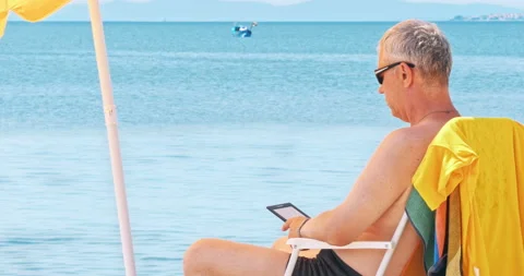 Mature man at the beach reading electronic reader Stock Footage 94172622