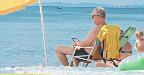 Mature man at the beach reading electronic reader Stock Footage 94964596