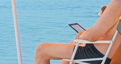 Mature man at the beach reading electronic reader Stock Footage 96506871