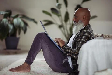 Mature man with beard using laptop on floor Foto stock