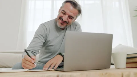 Mature man with beard working intently working on a laptop on sofa in a bright Video stock 292853510