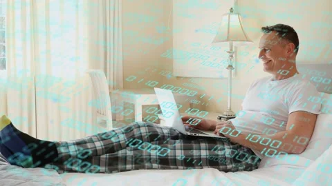 Mature man on bed typing on laptop for remote work, shifting, laughing as binary Stock Footage 332981877