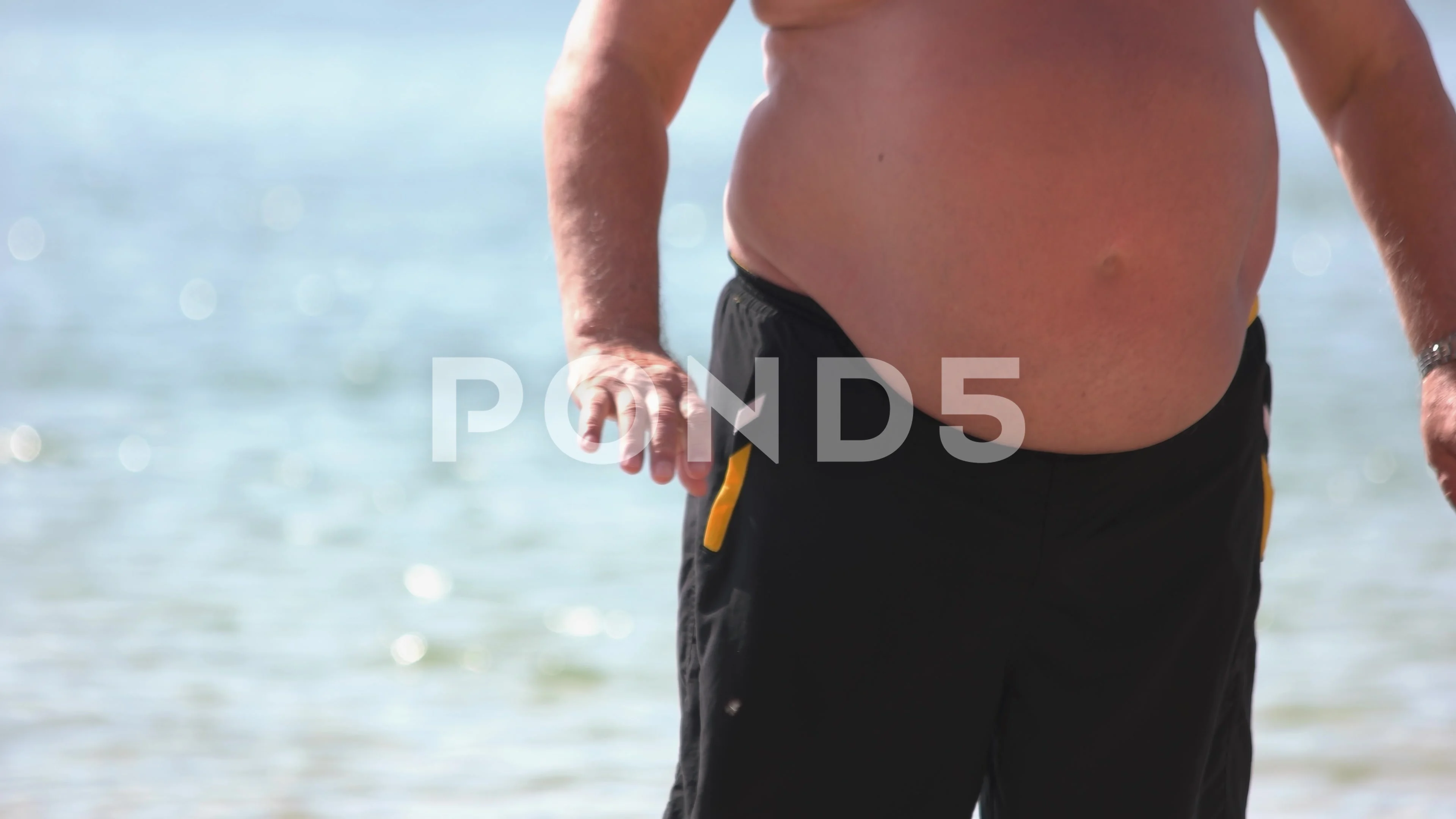 Mature man with belly fat standing on the beach.