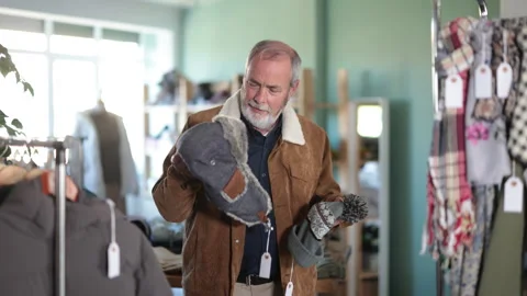 Mature man choosing a warm hat for the winter in a clothing store. Pensioner Vídeo Stock 326319574