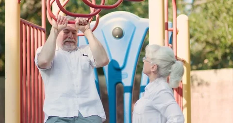 Mature man does pullups on a playground gym wife cheers him on Stock Footage 115953181