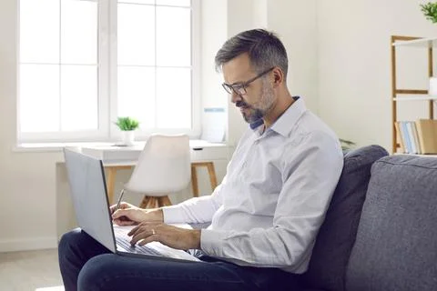 Mature man doing remote work working on laptop in his home office making notes Stock Photos
