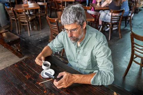 Mature man drinking coffee using smartphone in cafe Stock Photos