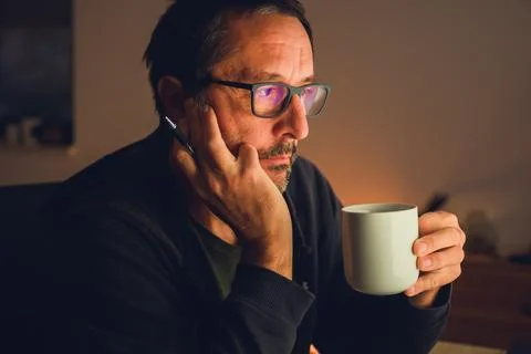 Mature man drinking coffee while looking at computer screen in dark room wi.. Stock Photos